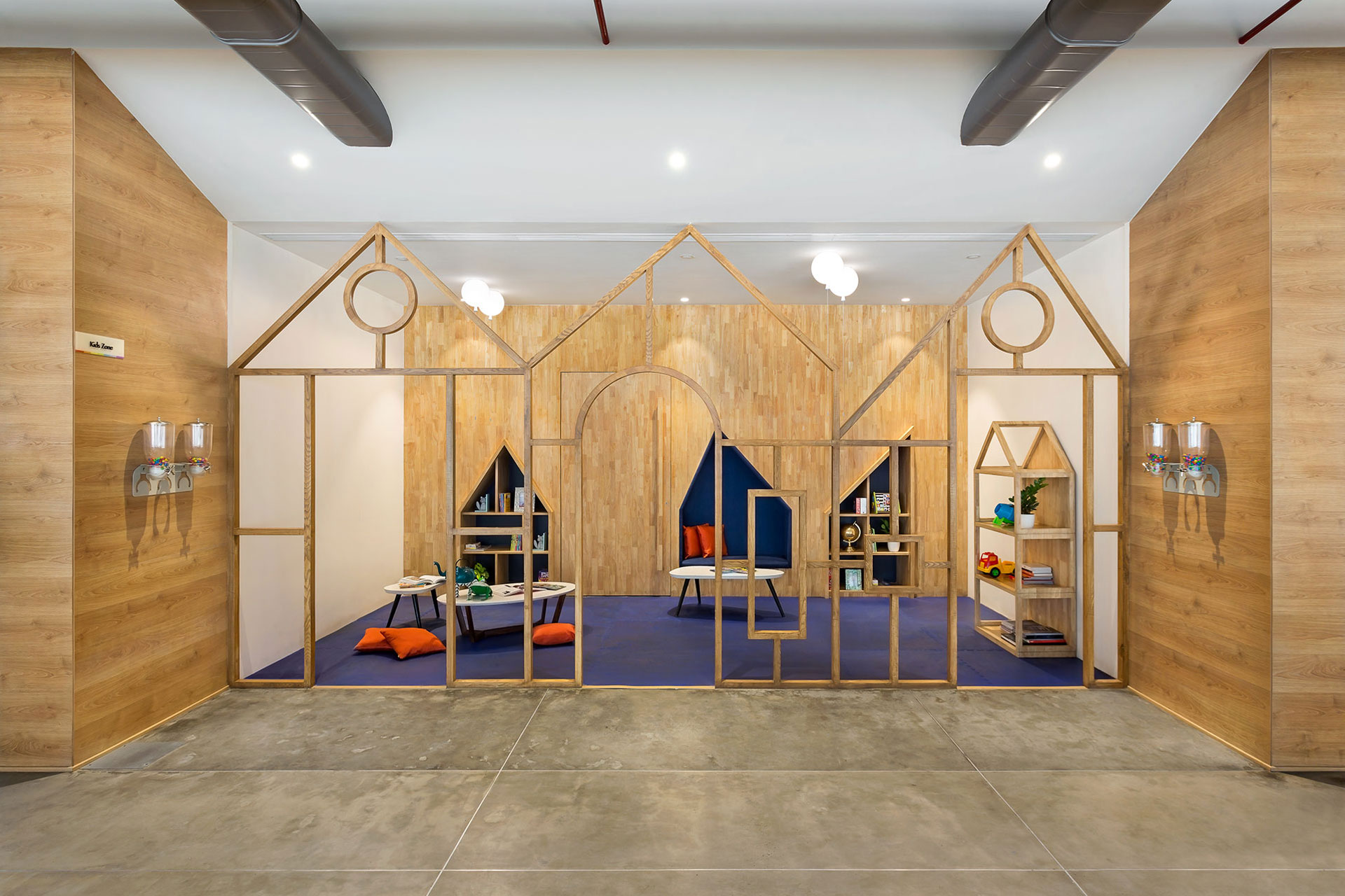 Kids’ play area set within two flanking RC walls clad in wood has a playful built-in niche set in the back storage wall with smaller niches created as seating and book shelves. The blue colored floor visually creates a lively setting for the play area.